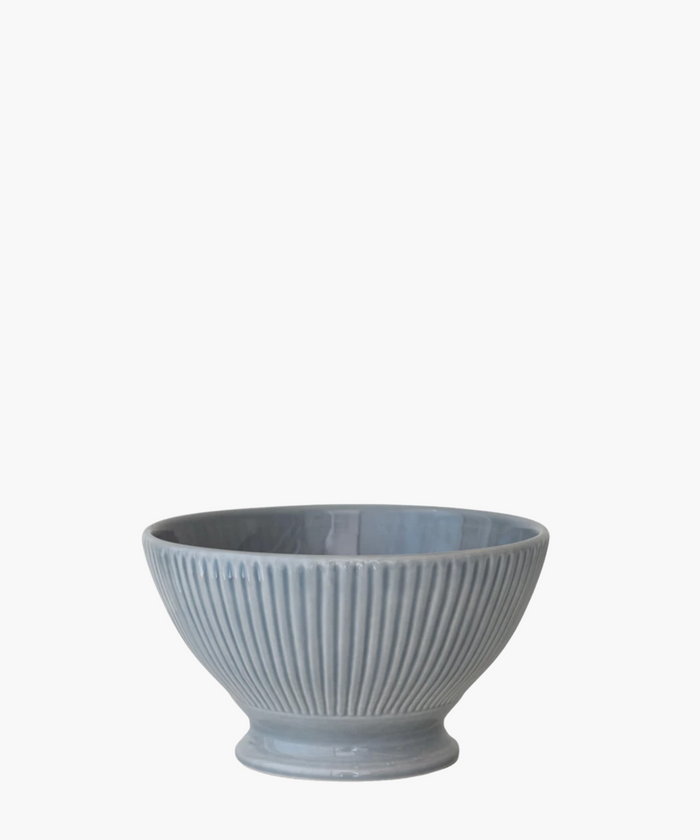 A ribbed, light blue ceramic bowl with a wide top and narrow base is centered against a white background, conveying a simple and elegant tone. | Wildwood Home Co.