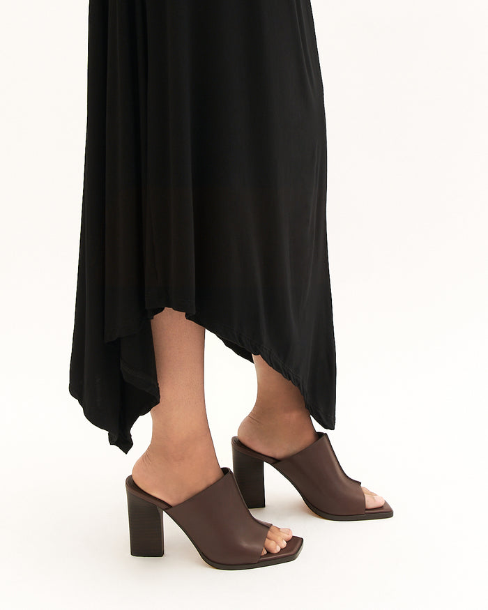 Brown open-toe heeled shoes worn with a black dress on a white background