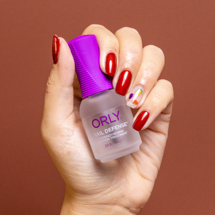Hand holding an ORLY Nail Defense treatment bottle against a brown background