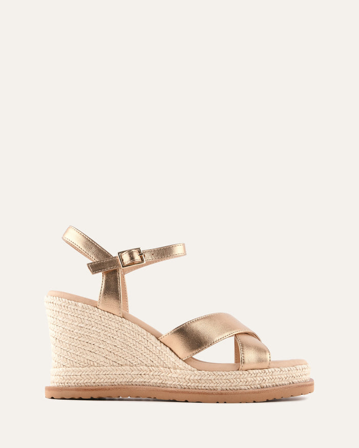 Gold wedge sandal with espadrille sole on a light gray background