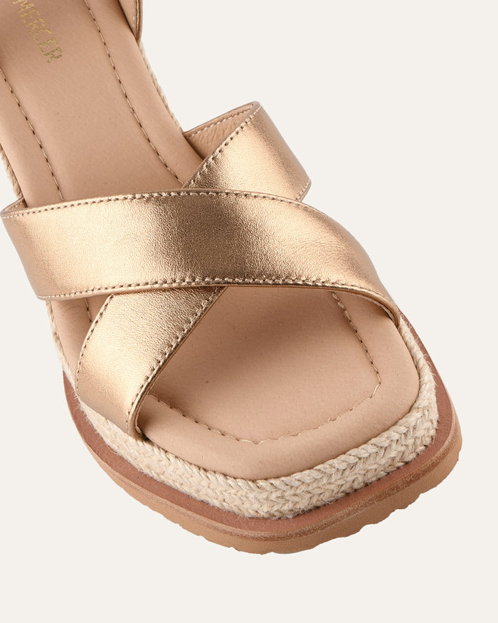 Gold sandal with espadrille sole on a white background
