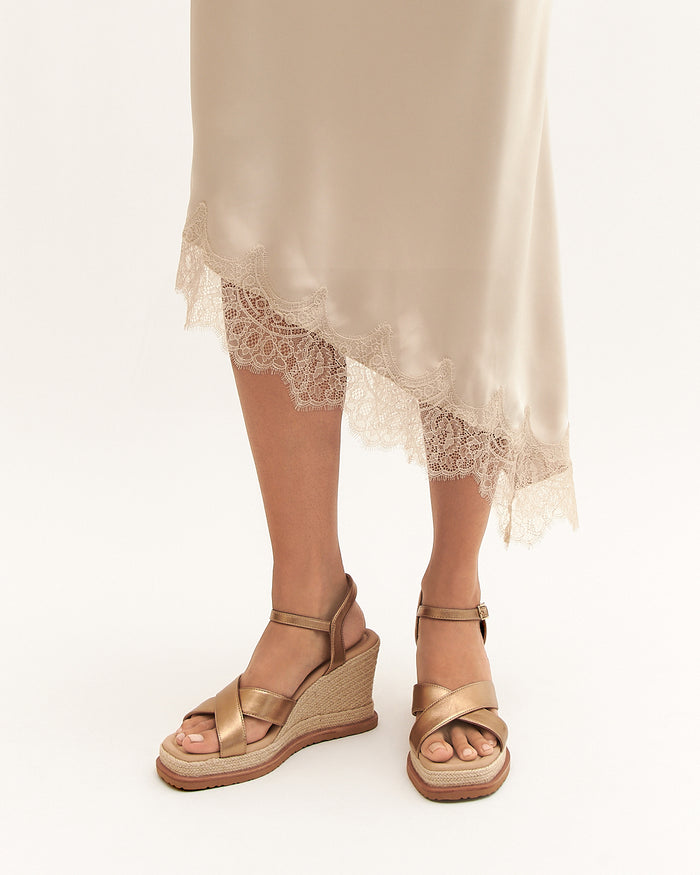 Gold wedge sandals worn with a beige skirt on a white background