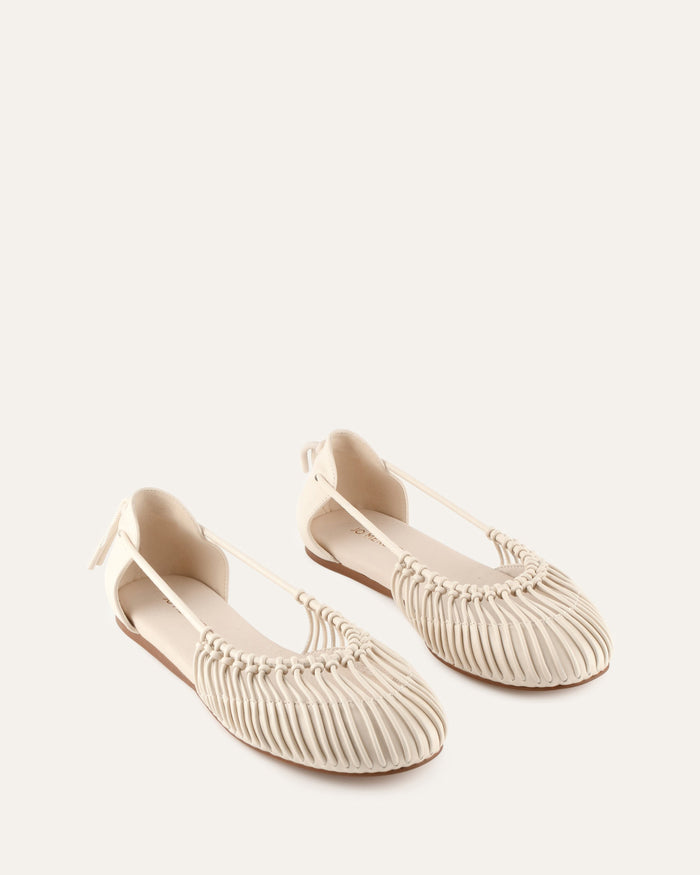 Pair of beige ballet flats with decorative straps on a light background