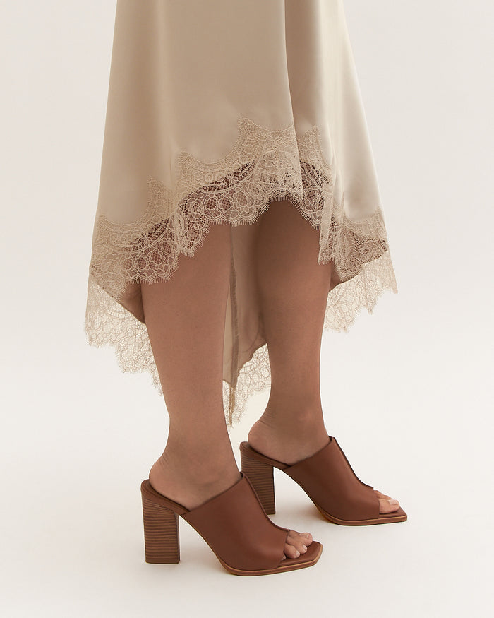 Brown open-toe shoes worn with a beige skirt on a white background